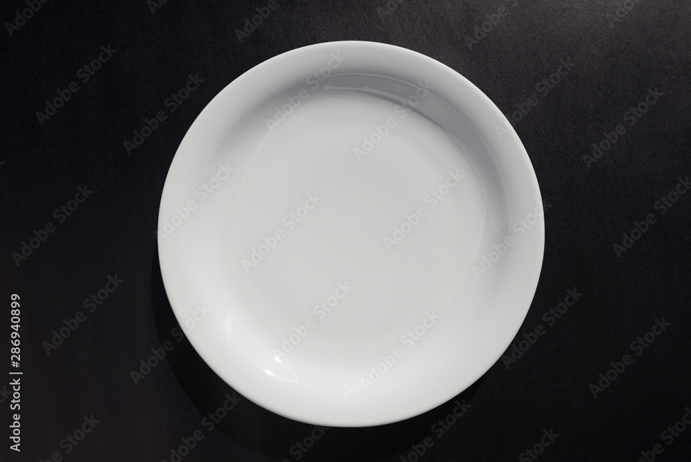 White ceramic round plate on black background White ceramic round plate on black background