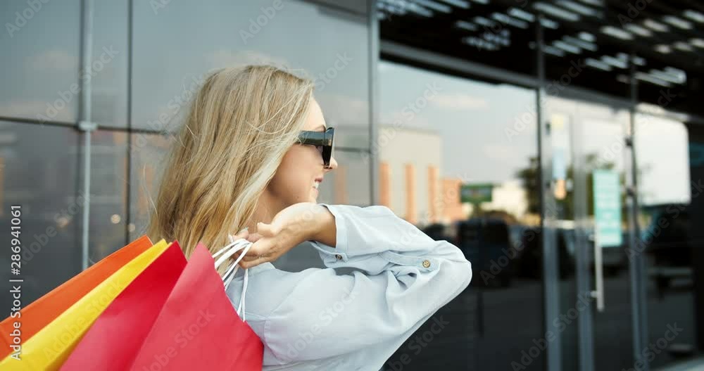 Beautiful blonde woman in sunglasses and casual outfit holding paper bags and smiling to camera, shopping Beautiful blonde woman in sunglasses and casual outfit holding paper bags and smiling to camera, shopping