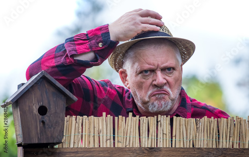 An evil, aggressive man watches his neighborhood over the garden fence. Concept dispute and aggression between people. photo