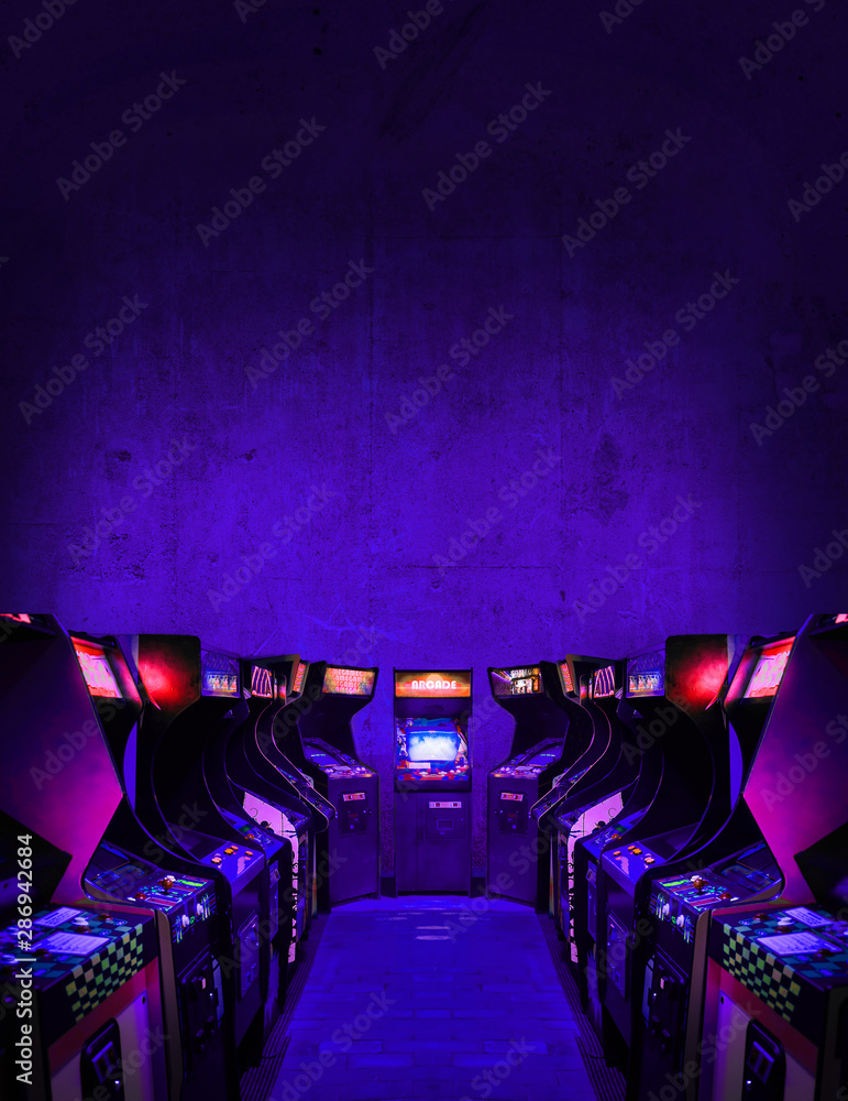 Old Unbranded Vintage Arcade Video Games in dark gaming room with purple light with glowing displays and concrete wall - vertical photo of retro design with free copy space for a poster or magazine