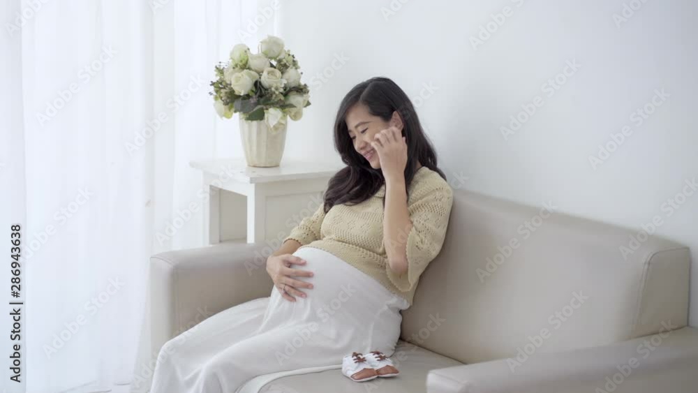 image of smiling pregnant woman sitting on sofa and touching belly image of smiling pregnant woman sitting on sofa and touching belly