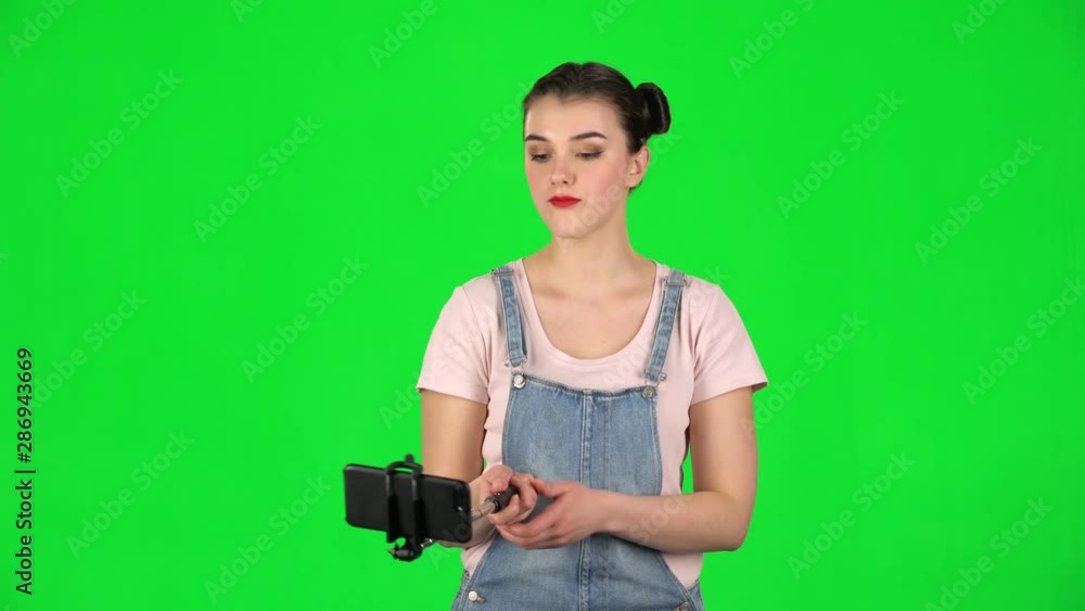 Girl makes selfie on mobile phone using selfie stick on green screen Girl makes selfie on mobile phone using selfie stick on green screen