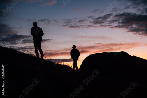  Two silhouettes walk on slope towards sunset