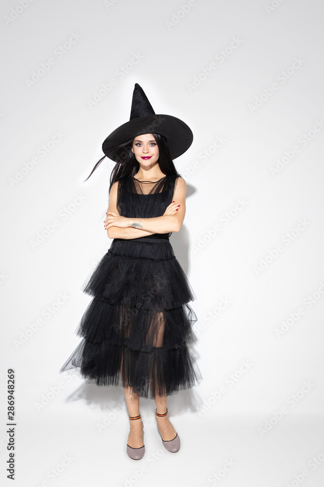 Young brunette woman in black hat and costume on white background. Attractive caucasian female model. Halloween, black friday, cyber monday, sales, autumn concept. Copyspace. Dancing, posing. Young brunette woman in black hat and costume on white background. Attractive caucasian female model. Halloween, black friday, cyber monday, sales, autumn concept. Copyspace. Dancing, posing.