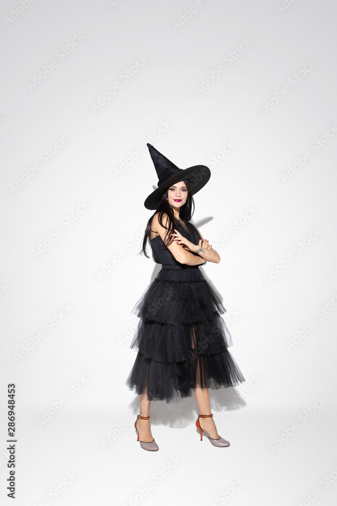 Young brunette woman in black hat and costume on white background. Attractive caucasian female model. Halloween, black friday, cyber monday, sales, autumn concept. Copyspace. Standing hands crossed. Young brunette woman in black hat and costume on white background. Attractive caucasian female model. Halloween, black friday, cyber monday, sales, autumn concept. Copyspace. Standing hands crossed.