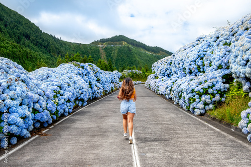 Azores, Young woman running in the middle of road with white and blue hydrangea at the roadside in Lagoa Sete Cidades (Seven Cities Lagoon), São Miguel, Açores photo