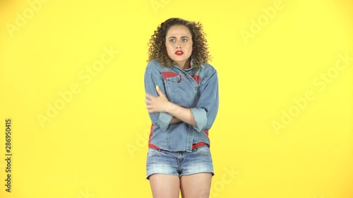 Beautiful girl froze and trying to keep warm on yellow background at studio.