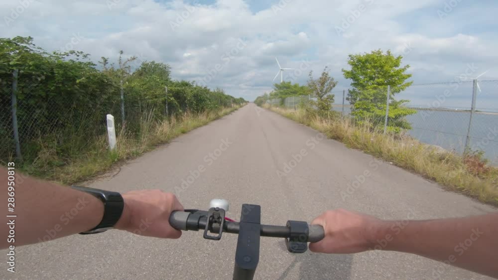 Driving electric scooter on road with windmills in the background Driving electric scooter on road with windmills in the background