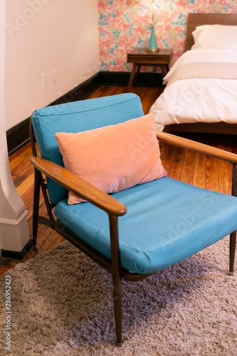 Blue cushion and wood mid century modern chair with pink pillow in bedroom, vintage pink floral wallpaper