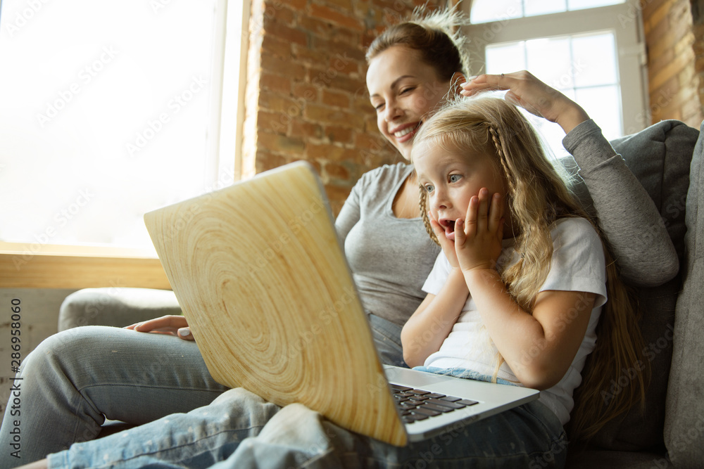 Female caucasian teacher and little girl, or mom and daughter. Homeschooling. Sitting on the sofa and using laptop for knowledges getting while lesson is. Education, school, studying concept. Female caucasian teacher and little girl, or mom and daughter. Homeschooling. Sitting on the sofa and using laptop for knowledges getting while lesson is. Education, school, studying concept.
