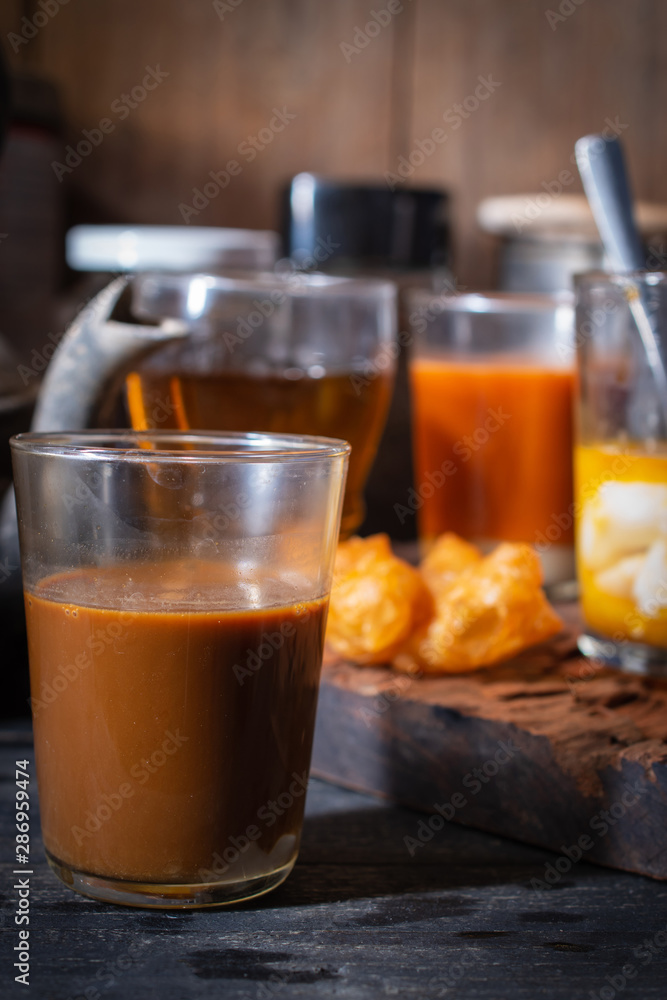 Traditional Thai hot coffee with milk on the wood table there are Traditional Thai hot tea with milk, deep-fried doughstick (patongko), hot tea and soft-boiled egg plated around. Traditional Thai hot coffee with milk on the wood table there are Traditional Thai hot tea with milk, deep-fried doughstick (patongko), hot tea and soft-boiled egg plated around.