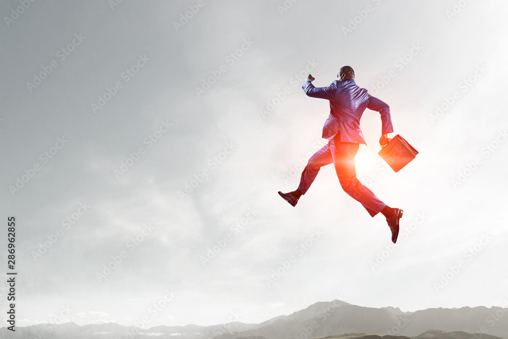 back view of running black businessman with briefcase against mountain and sky landscape background