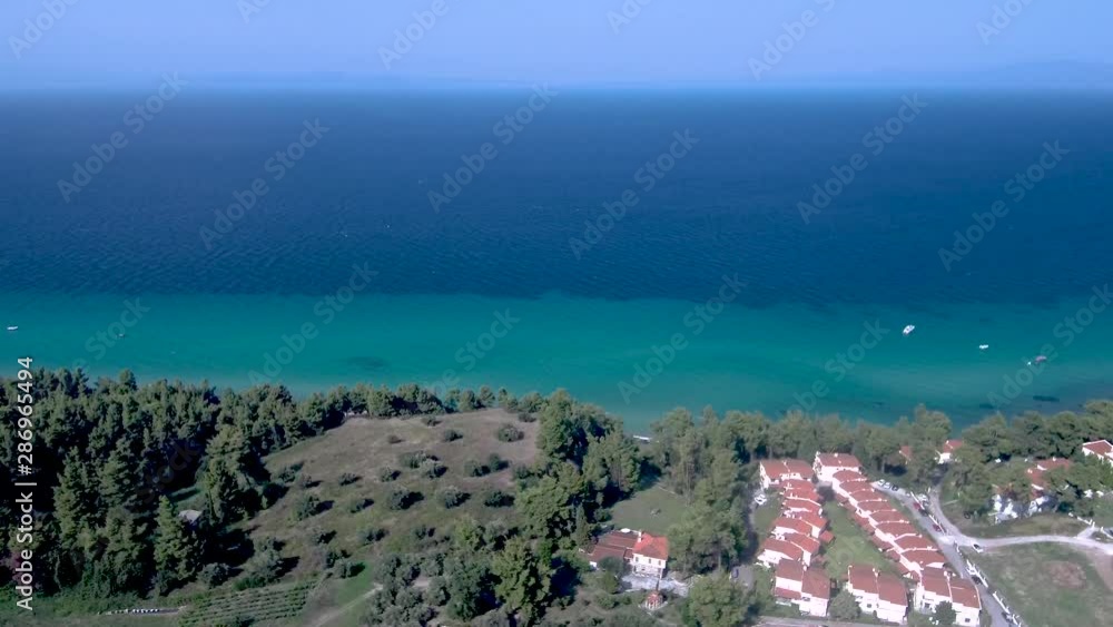 Aerial view of turquoise and blue sea coast and tourist homes in Kriopigi, Halkidiki Greece, moving forward by drone