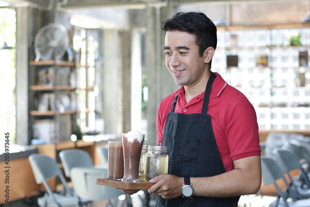 close up asian man barista smiling holding tray with coffee on it and cafe as background. cafe owner standing in restaurant close up asian man barista smiling holding tray with coffee on it and cafe as background. cafe owner standing in restaurant
