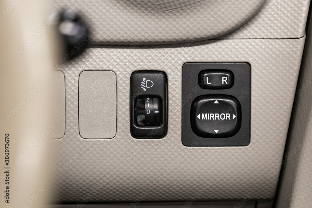 Close-up on the headlight and side mirror switch control buttons, automatic adjust level dashboard. modern car interior: parts, buttons, knobs. Close-up on the headlight and side mirror switch control buttons, automatic adjust level dashboard. modern car interior: parts, buttons, knobs.