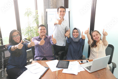 Young creative employees posing on camera in conference room. Company colleagues ready for open brainstorming session, group of multi ethnic business workers smiling at camera, multiple ethnic group photo
