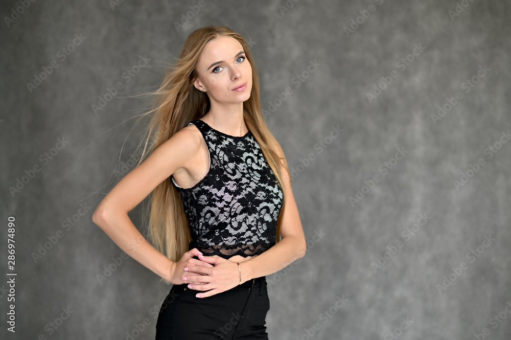 Portrait of a beautiful pretty girl in a gray T-shirt with long curly hair on a gray background. Beauty and brightness. Shows hands to the side, smiles with different emotions. Portrait of a beautiful pretty girl in a gray T-shirt with long curly hair on a gray background. Beauty and brightness. Shows hands to the side, smiles with different emotions.