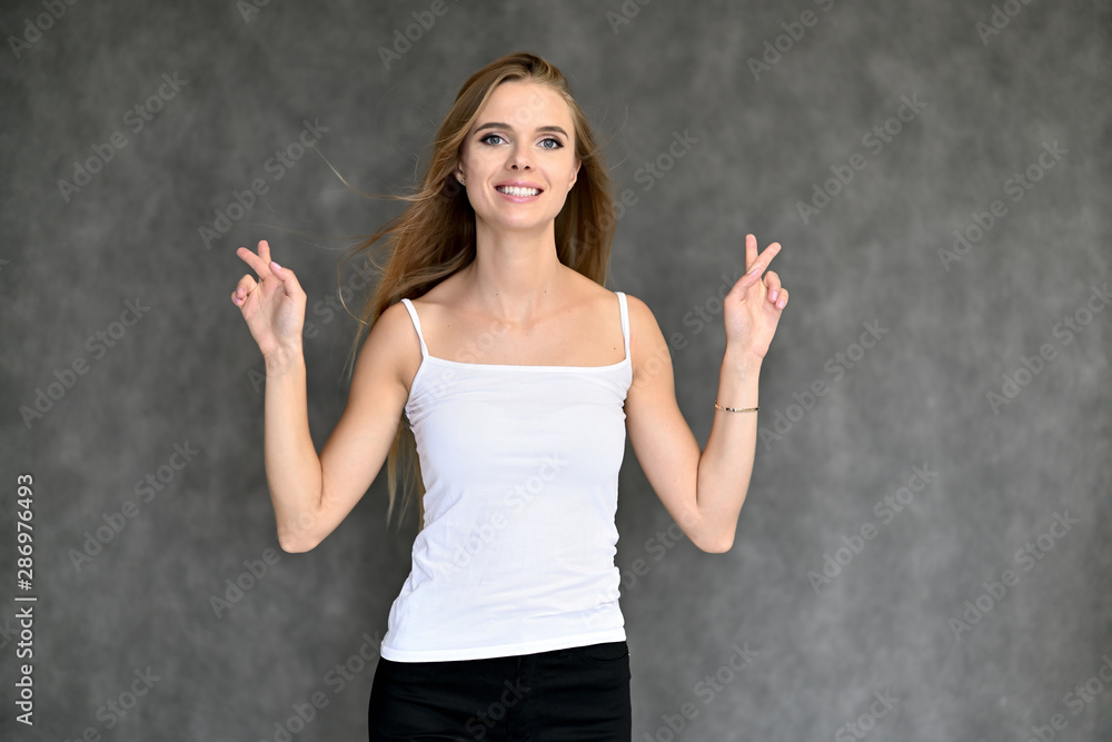 Portrait of a beautiful pretty girl student in a white T-shirt with long curly hair on a gray background. Beauty and brightness. Shows hands to the side, smiles with different emotions. Portrait of a beautiful pretty girl student in a white T-shirt with long curly hair on a gray background. Beauty and brightness. Shows hands to the side, smiles with different emotions.