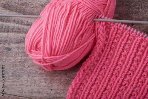 knitting sweaters, or a scarf with a red pattern, thin knitting needles on a white wooden background. Close-up. Copy space.