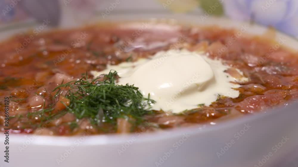 Bowl of homemade red borscht with smetana rotating. Portion of traditional Ukrainian Russian sour soup closeup. Bowl of homemade red borscht with smetana rotating. Portion of traditional Ukrainian Russian sour soup closeup.