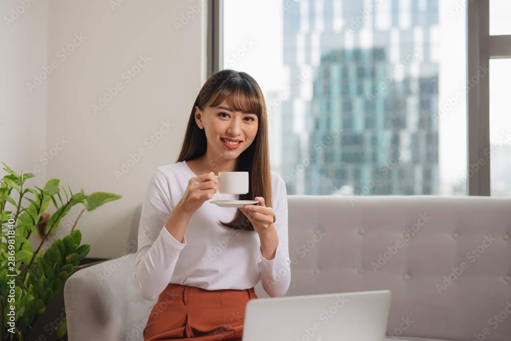Girl drinking morning coffee and using laptop while siting on couch Girl drinking morning coffee and using laptop while siting on couch