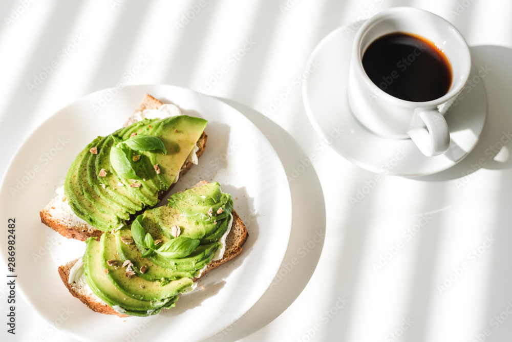 Avocado toasts and a cup of black coffee on a white table.