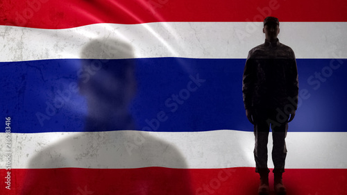 Thai soldier silhouette standing against national flag, proud army sergeant