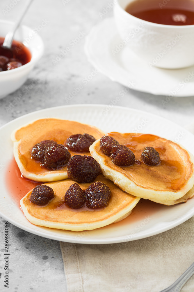Pancakes with strawberry jam on a white plate. Gray background Pancakes with strawberry jam on a white plate. Gray background