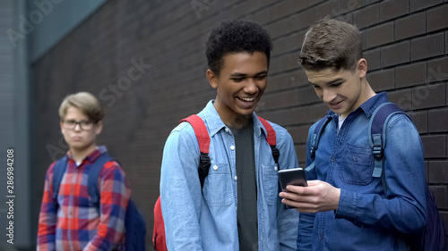 Two bully boys posting offensive video about upset guy behind, cyberbullying photo