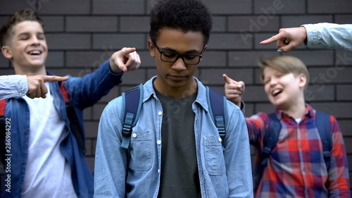 Tableau sur toile Group of cruel teenagers pointing fingers at black boy, humiliation and racism