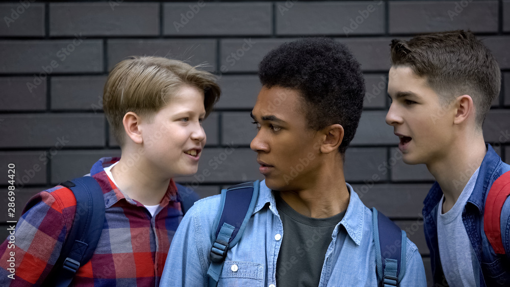 Evil students teasing black boy face-to-face, telling insults, racial bullying Evil students teasing black boy face-to-face, telling insults, racial bullying