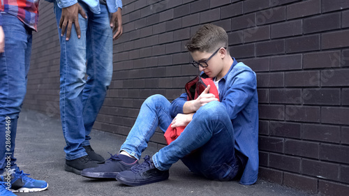 Teen boy leaning against wall, scared of bully students, intimidation at school