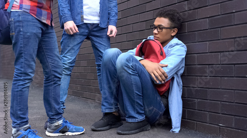 Black boy leaning against wall, scared of bully students, racial discrimination