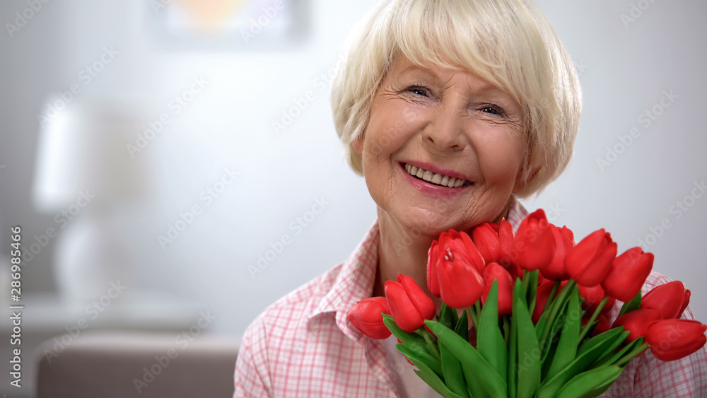 Beautiful old woman with bunch of flowers smiling at camera, birthday gift Beautiful old woman with bunch of flowers smiling at camera, birthday gift