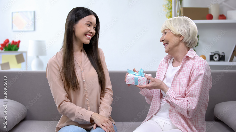 Grateful old woman holding birthday gift sitting with granddaughter, anniversary Grateful old woman holding birthday gift sitting with granddaughter, anniversary