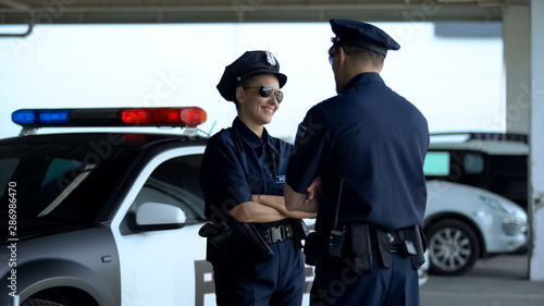 Male and female police officers smiling communicating on parking lot, on duty