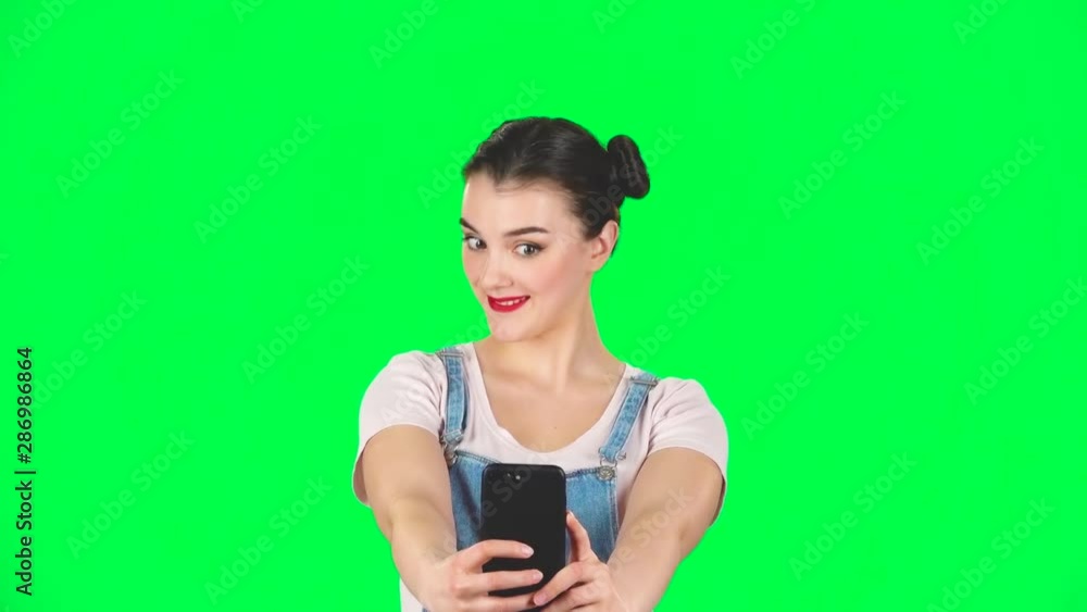 Young woman makes selfie on mobile phone then looking photos on green screen, slow motion