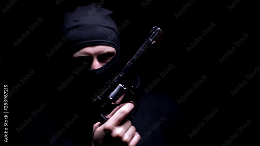 Dangerous man in balaclava mask holding gun, black background, serial killer Dangerous man in balaclava mask holding gun, black background, serial killer