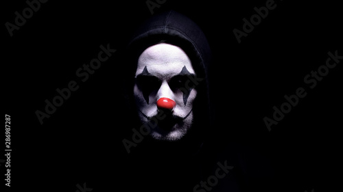 Foto Spooky clown in hoodie looking at camera, black background, criminal disguise