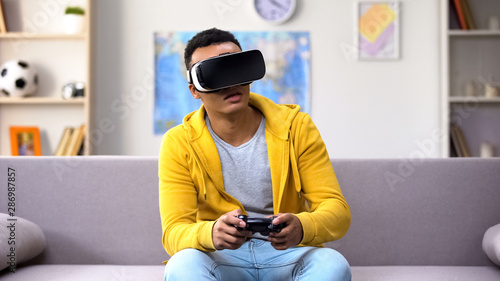 Emotional mixed-race guy in VR headset playing video game, reality simulation © motortion