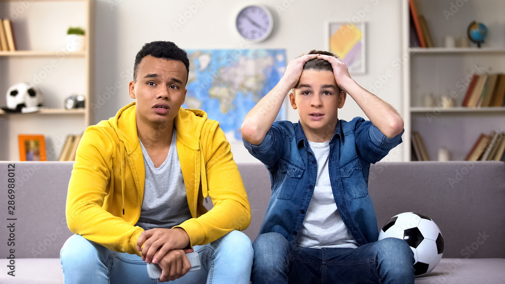 Anxious teenagers watching football match on TV unhappy with team losing, sport