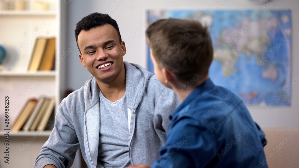 Multiracial teenagers making up after quarrel, smiling friends sitting on sofa Multiracial teenagers making up after quarrel, smiling friends sitting on sofa