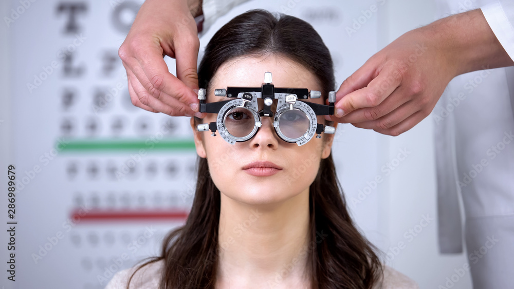 Oculist putting optical trial frame on girl sight correction diopter measurement Oculist putting optical trial frame on girl sight correction diopter measurement