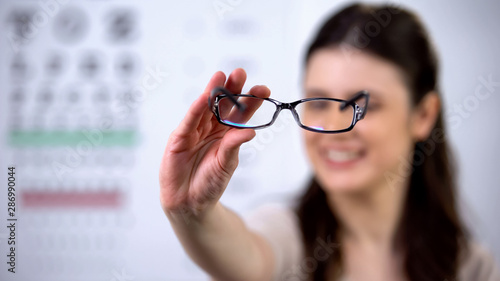 Fototapeta Naklejka Na Ścianę i Meble -  Cheerful female optometrist patient showing new eyeglasses, sight correction
