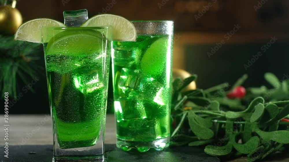 Panoramic shooting of green cocktails in glass glasses. On the edge of the glass to put a slice of lime. A cube of cold ice floats in the glass. Christmas drink on the background of Christmas tree Panoramic shooting of green cocktails in glass glasses. On the edge of the glass to put a slice of lime. A cube of cold ice floats in the glass. Christmas drink on the background of Christmas tree