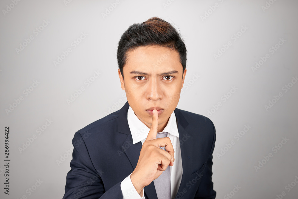 Young Asian businessman showing a sign of silence gesture putting finger in mouth Young Asian businessman showing a sign of silence gesture putting finger in mouth