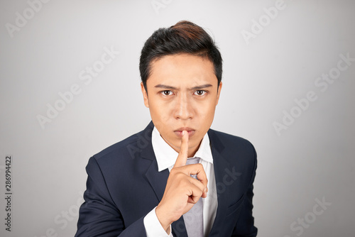 Young Asian businessman showing a sign of silence gesture putting finger in mouth