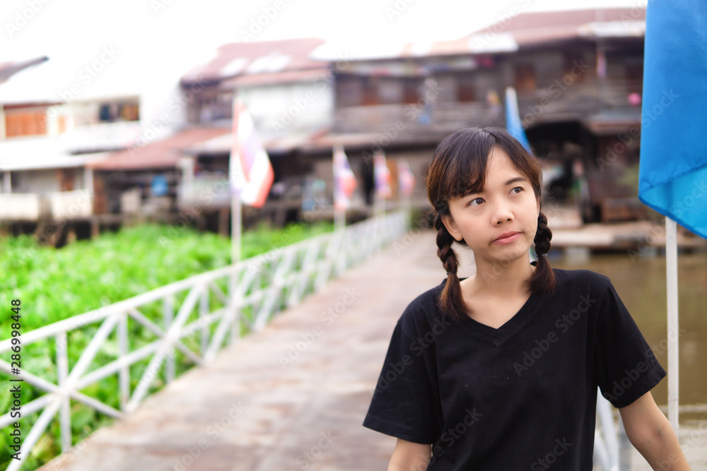 Braid young Asian woman doubt on the bridge with Thai flag behind wooden house in the background