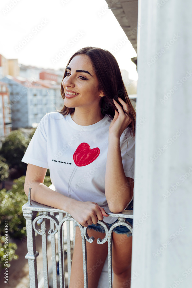 Beautiful brunette girl standing on the balcony on a sunny day and looking away Beautiful brunette girl standing on the balcony on a sunny day and looking away