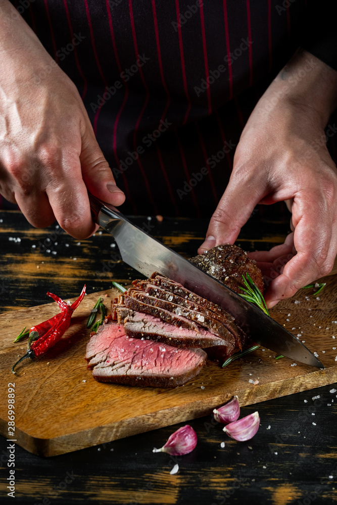 Chef hands slicing beef steak with knife on wood cutting desk. Top view food preparation process concept.